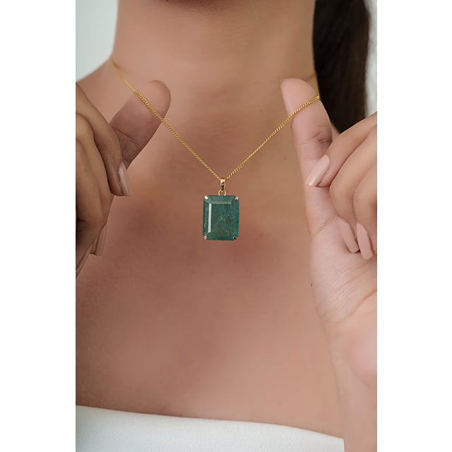This elegant pendant showcases a striking 14.22 carat natural emerald set in 14K yellow gold. The emerald measuring...