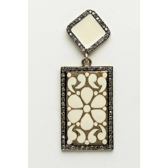 Pair of fascinating dangle earrings in white enamel with a floral and paisley design. Bordered with round, brilliant cut...