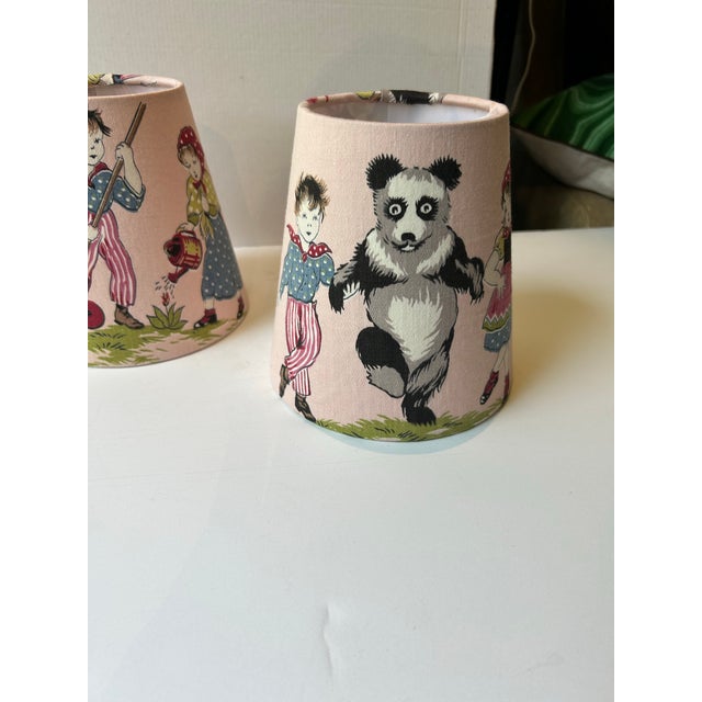 A pair of lampshades handmade from a charming scene of kids dancing and gardening with a panda. Measurements: top 4”...