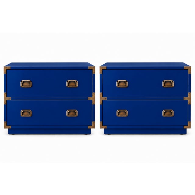 A striking pair of campaign-style nightstands with a vivid blue finish and warm brass-tone hardware. Each nightstand has...