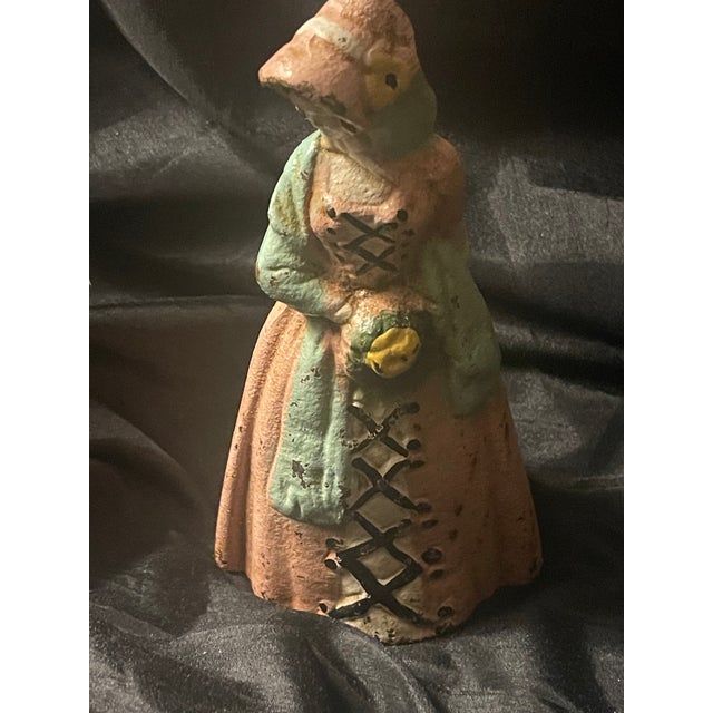 This antique original cast iron doorstop featuring a colonial or Victorian lady in a peachy pink dress and sunflower...