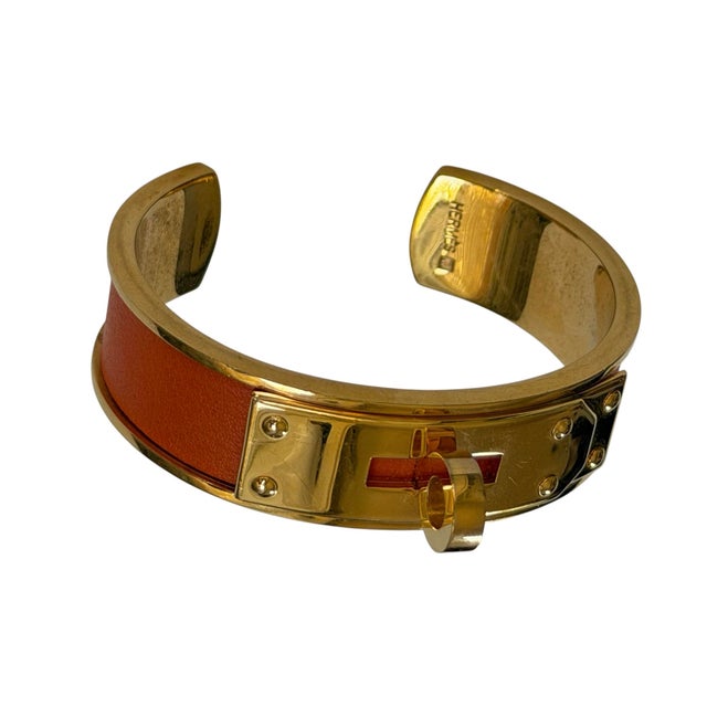 This timeless Kelly Bangle is in excellent condition. This luxurious piece features gold-plated hardware and orange...