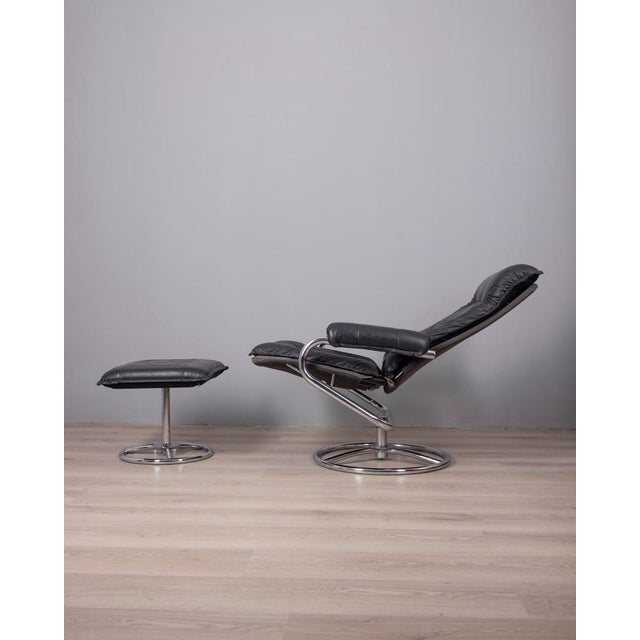 Armchair with footrest, chromed tubular metal frame and black leather upholstery, the armchair is reclining, Italian...