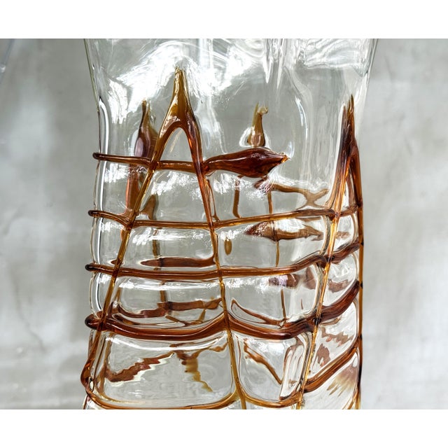 Executed in thick clear hand-blown glass with dramatic applied amber glass threading, the vase presents an architectural...