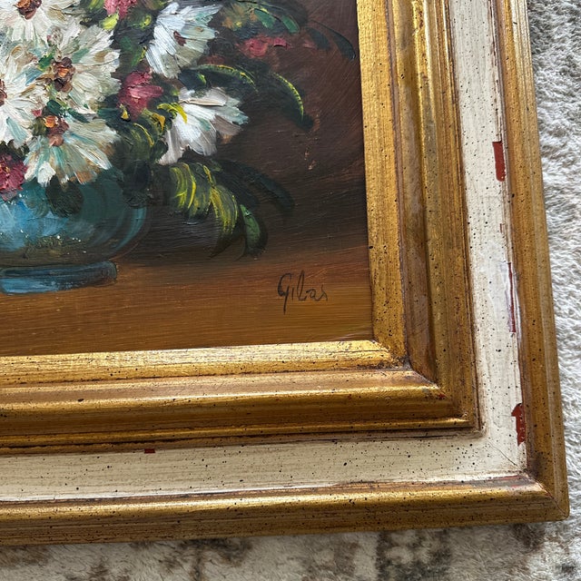 A vintage framed still-life oil painting featuring a bouquet of white daisies and small pink/red flowers in a blue vase,...