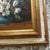 A vintage framed still-life oil painting featuring a bouquet of white daisies and small pink/red flowers in a blue vase,...