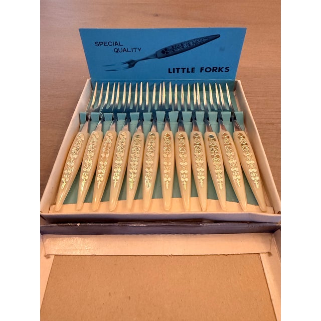 Great piece of history in its original box! Set of 12 tiny forks made of stainless steel and plastic. The ivory colored...
