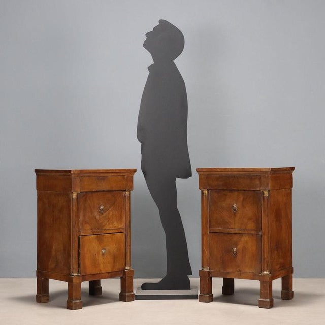 Pair of Empire walnut bedside tables. A projecting drawer in the lower section is supported by turned half-columns with...