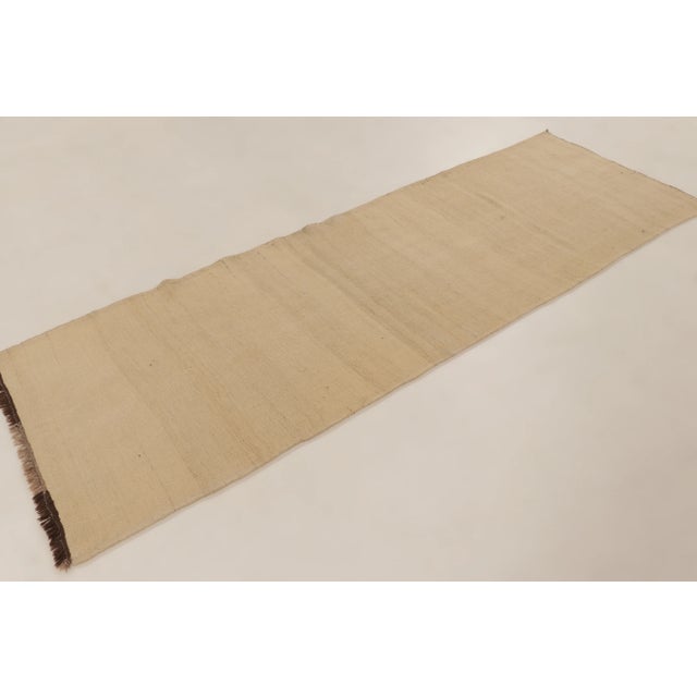 Handwoven in wool, this 3x9 Rez Kilim presents a quiet design of ivory tones enriched by subtle striations and natural...