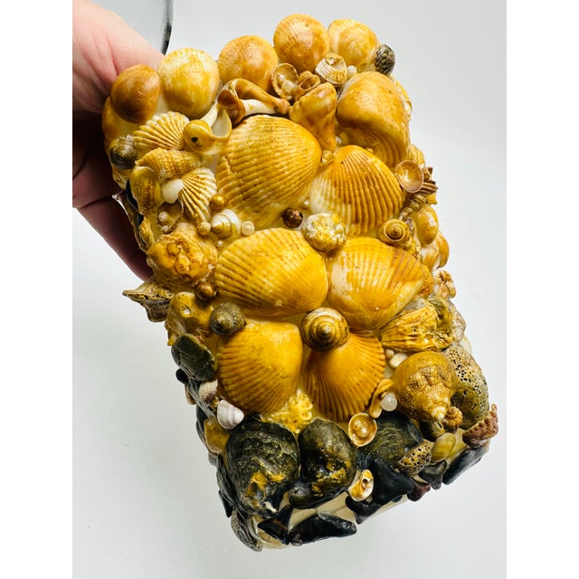 This is a vintage-inspired shell-covered vase. It has a highly textured and ornate surface, densely encrusted with an...