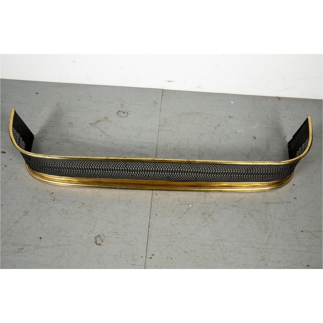 A long, curved fireplace fender with a serpentine (bowed) front and rolled brass top rail and base and pierced iron panel...