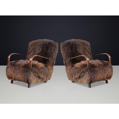 An iconic pair of 1940s halabala lounge chairs, newly upholstered in rich dark dutch sheepskin, combining sculptural...