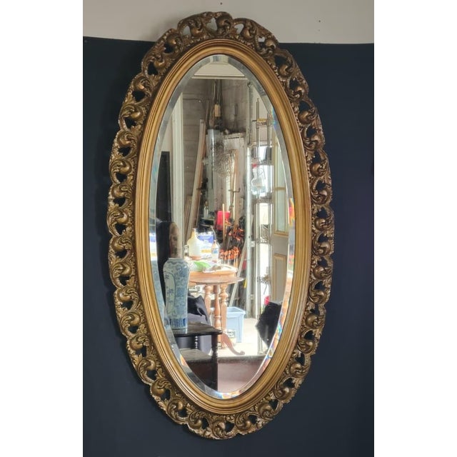 Elegant early 1900s French style oval wall mirror featuring a hand-carved gilt frame with intricate decorative details and...