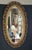 Elegant early 1900s French style oval wall mirror featuring a hand-carved gilt frame with intricate decorative details and...