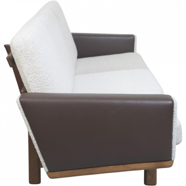 Hans Wegner GE236 sofa upholstered in Dedar Milano Boucle fabric with a frame of smoked oak and brown leather armrests....