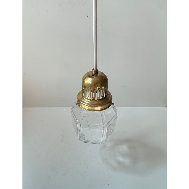 A 1930s ceiling light composed of a partially perforated brass top and set with a checkered grenade shaped clear glass...