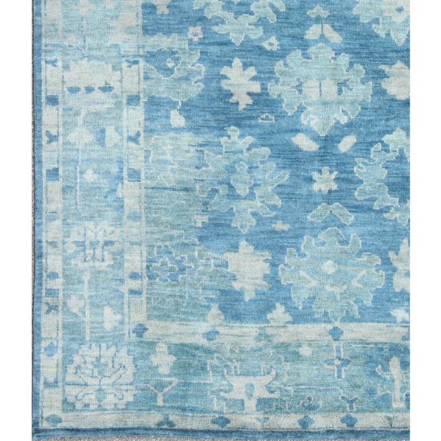 This modern Indian Oushak rug has been hand-knotted in wool and features an all-over, sub-geometric floral design rendered...