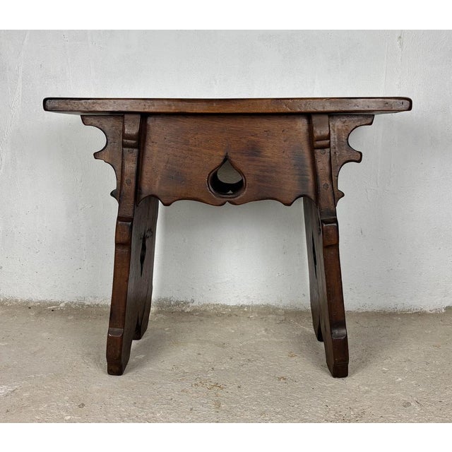 Rustic solid walnut stool or side table featuring hand-carved decorative cut-out details and a sculptural design. The...