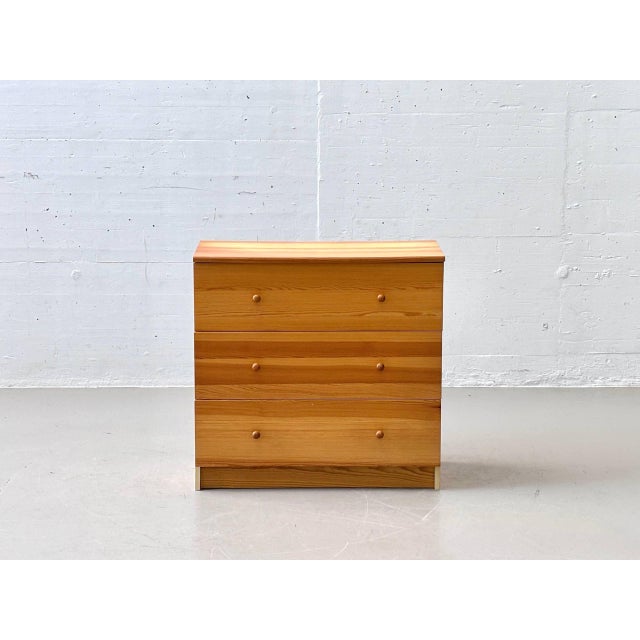A simple chest of drawers made of solid pine with a clean, scandinavian-inspired design and a warm wood tone. The...