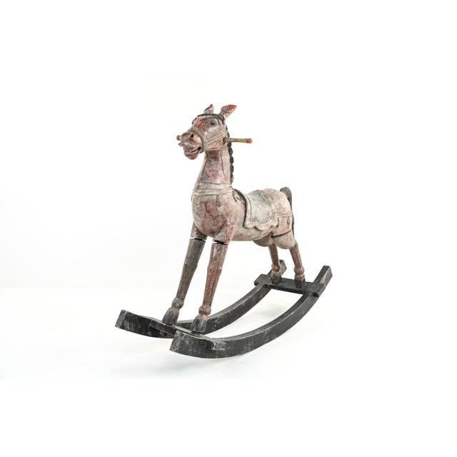 A carved and painted wooden rocking horse with a long neck, toothy expression, painted eyes, braided black mane and tail,...