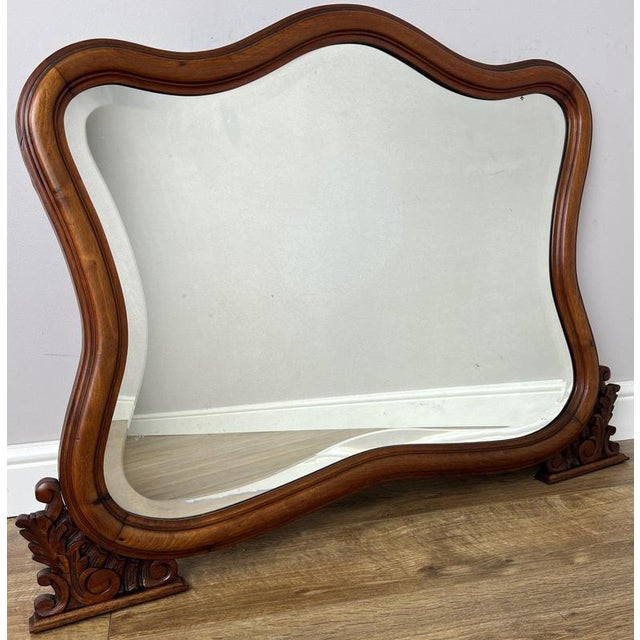 An elegant Antique French mirror with a beautifully flowing shaped frame, warm walnut finish and decorative carved scroll...