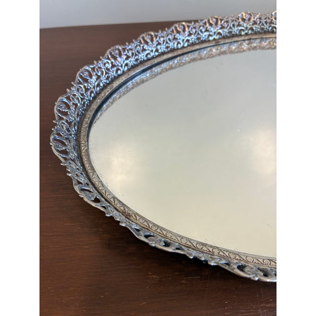 Elegant vintage silver tone mirrored tray featuring an ornate pierced gallery edge and classic Hollywood Regency styling....