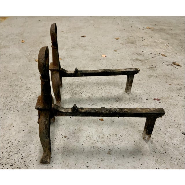 A pair of antique cast iron fireplace andirons with rust and dark oxidation, heavy oval ring finials, tapered columns,...