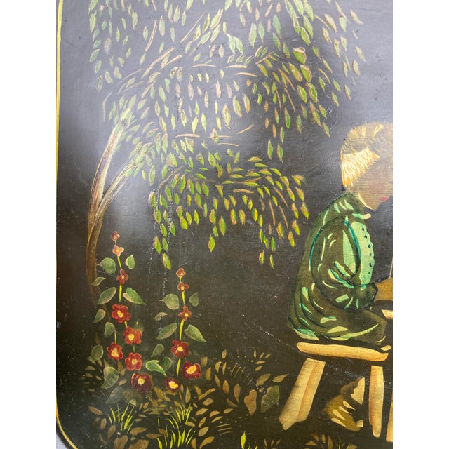 An early 20th Century tole painted tray of a couple eating at an outdoor table with their cat, surrounded by flowers and...