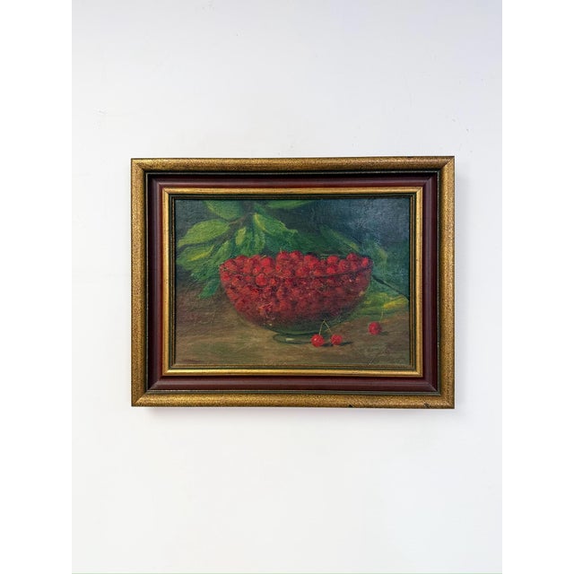 This antique oil painting presents a classic still life composition, featuring a glass bowl overflowing with ripe red...