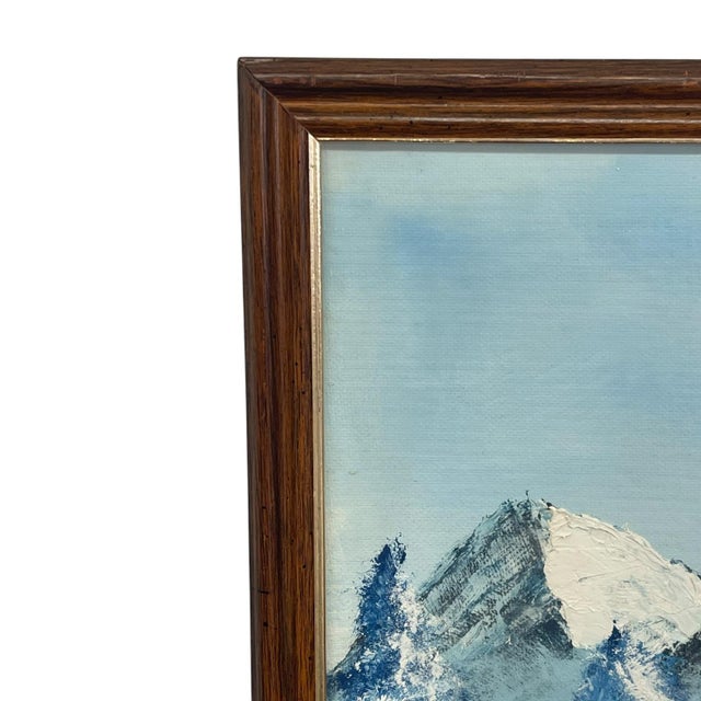Vintage framed landscape painting depicting a tranquil mountain lake bordered by evergreen trees with a dramatic range of...