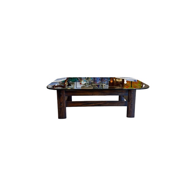 A striking 1970s vintage coffee table featuring a beautifully sculpted dark wood frame and a substantial smoked glass...