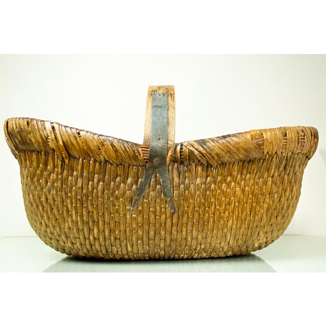 A mid-20th century Chinese woven reed gathering basket with a bentwood handle attached with simple iron straps....