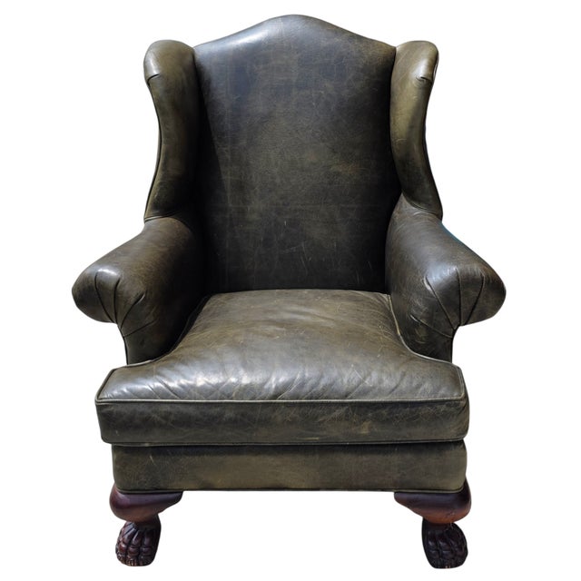 A handsome English Georgian-style wingback library armchair, upholstered in richly patinated distressed olive green...