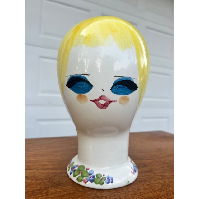 A hand painted female head, stylized with big blue eyes and blonde hair. This Italian ceramic piece can be used as a hat...