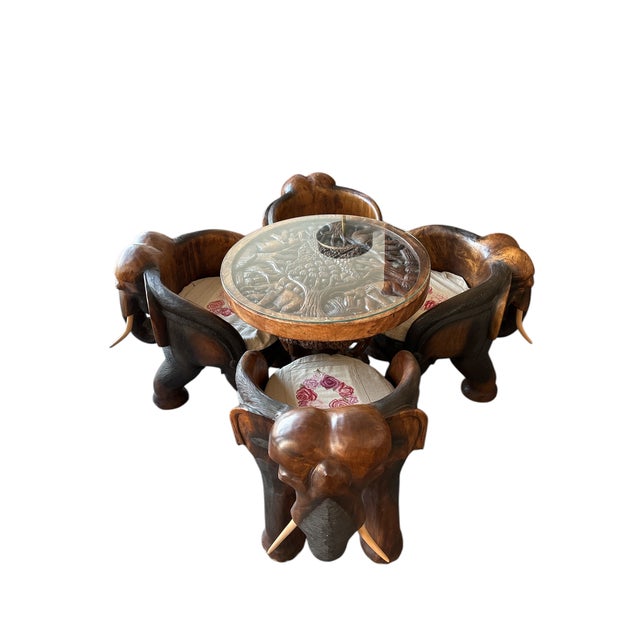 Hand-carved wooden table set featuring four elephant-shaped chairs and a round tabletop intricately carved with a jungle...