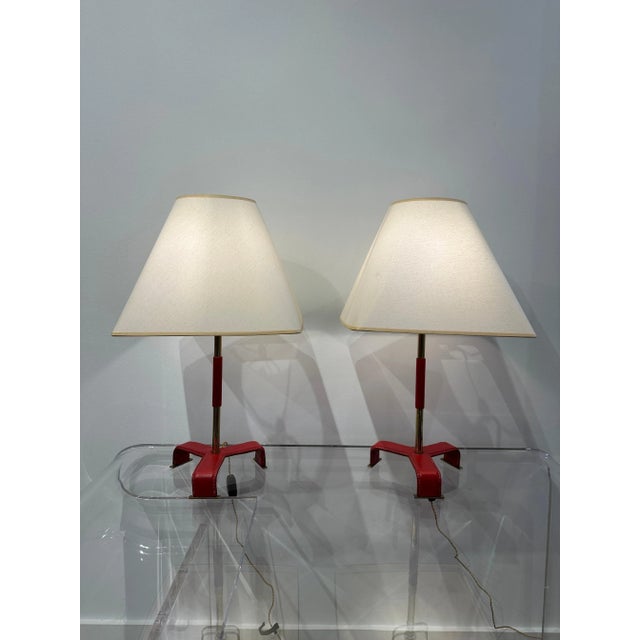 These vintage Jacques Adnet red stitched leather lamps with tri-pod style legs, leather strap to body. Fully updated...