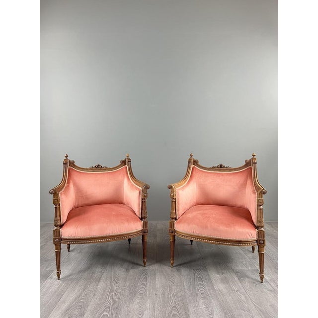An elegant pair of Louis XVI style bergère armchairs in carved and molded wood, resting on fluted, tapered legs. The...