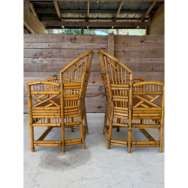 This pair of vintage rattan side chairs showcases classic Brighton Pavilion–style design with dramatic curved arms,...