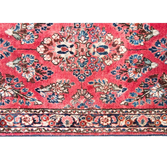 A petite early 20th century Persian Sarouk rug with a mirrored floral pattern across the field, surrounded by a simple...