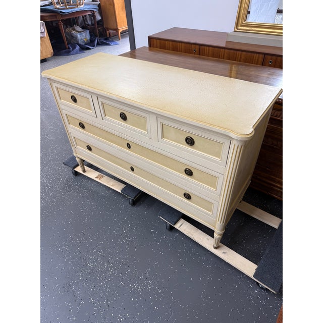 This is a French Louis XVI Creme Peinte Commode. It features a rectangular top with molded edges and turret corners, three...