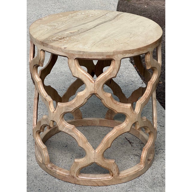 This is a versatile side table made from recycled elmwood. The table has a round top and a carved base with a repeating...