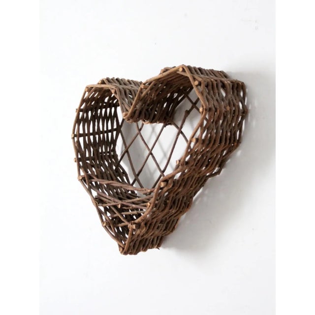 This vintage heart-shaped basket is handcrafted from natural twigs, creating a rustic and inviting piece. The open weave...
