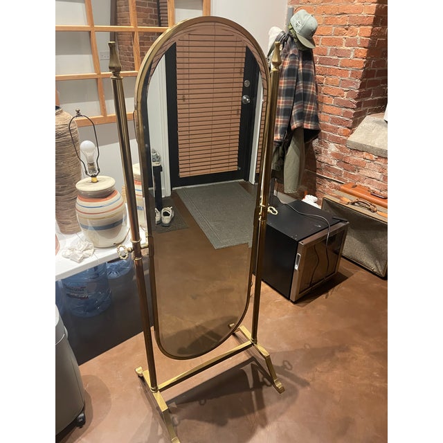 Elegant vintage brass cheval mirror featuring a classic oval glass set within a sculptural freestanding frame. The mirror...