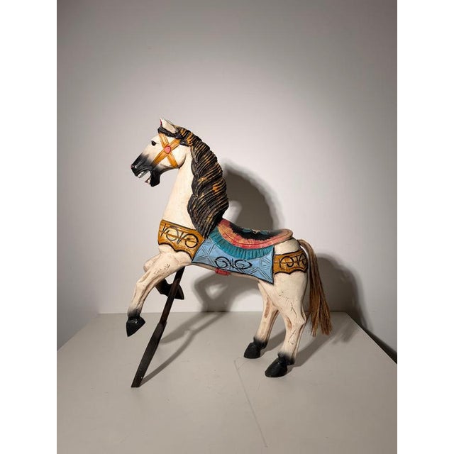 Decorative vintage carousel horse sculpture crafted in carved and painted wood, presented on a simple dark metal support....
