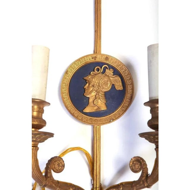 A pair of bronze two-light neoclassical wall sconces. Measurements: cm 48 x 22. Up to 250V (Europe/UK Standard).The wiring...