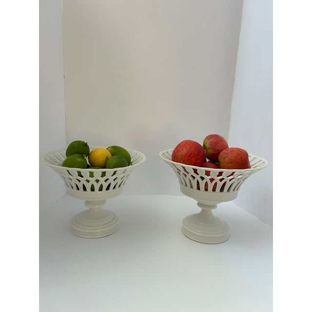 Two closely coordinated white glazed compotes with flared, pierced lattice bowls, scalloped rims, and stepped pedestal...