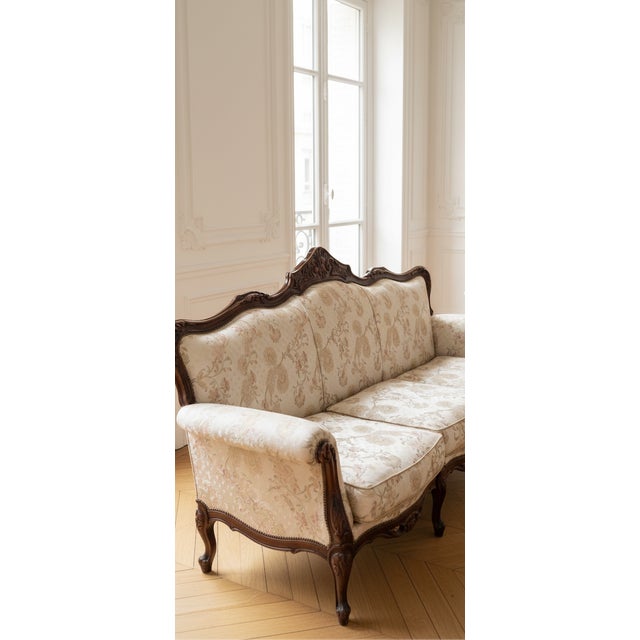 Vintage Victorian sofa and accent chair featuring ornate carved wood frame, camelback silhouette, and preserved floral...