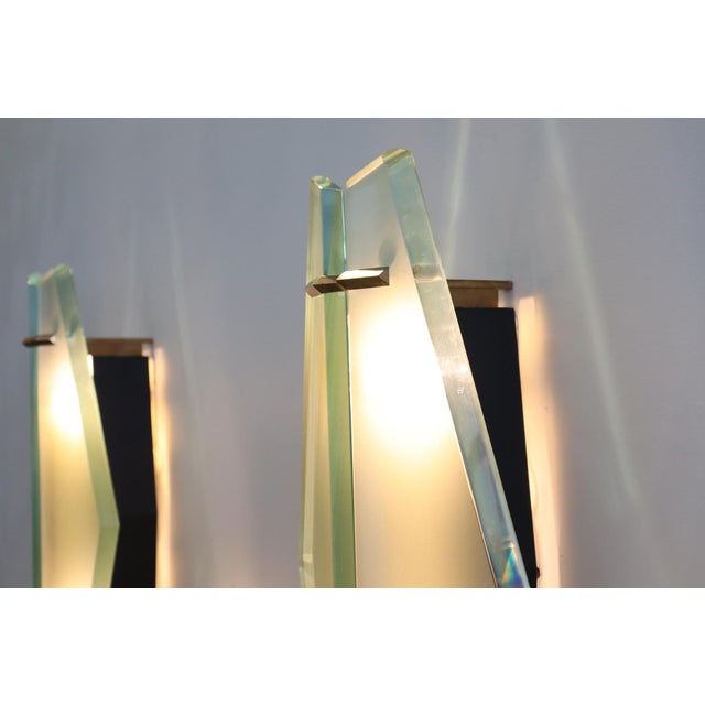 Large pair of 1943 model wall sconces, featuring a brass and metal frame and satin-finish glass shades with beveled edges,...