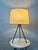 A sculptural mid-century modern tripod table lamp, featuring a slender blackened iron base accented with warm brass...