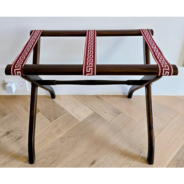 Handsome dark walnut folding luggage rack featuring three deep red and white Greek key woven straps that add a crisp,...